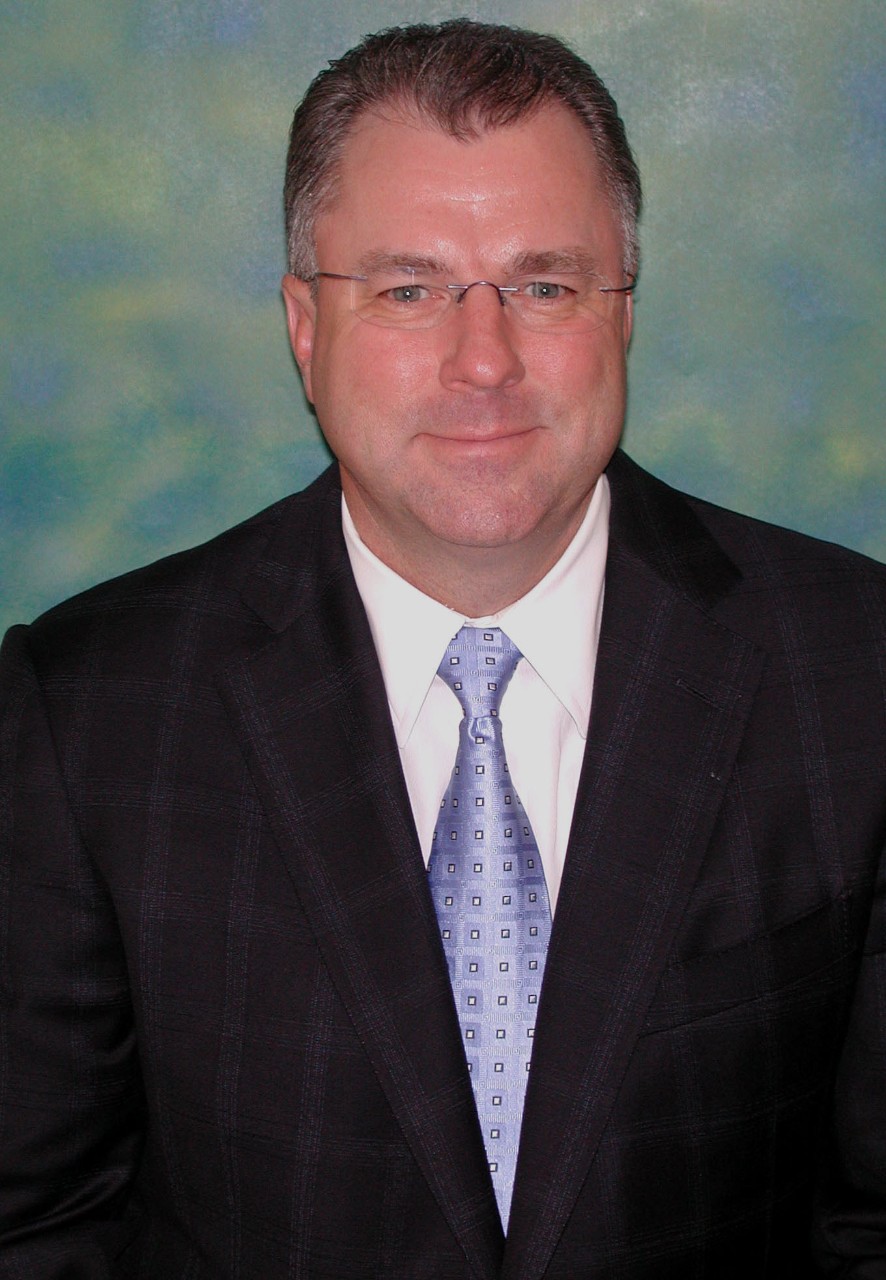 A man wears a dark suit and purple tie.