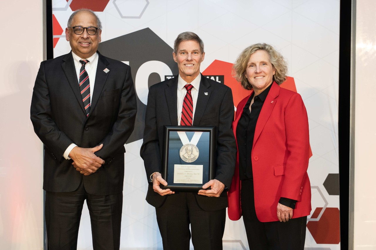 Rusty Myers holds an award and is flanked by President Pinto and Dean Lewis.