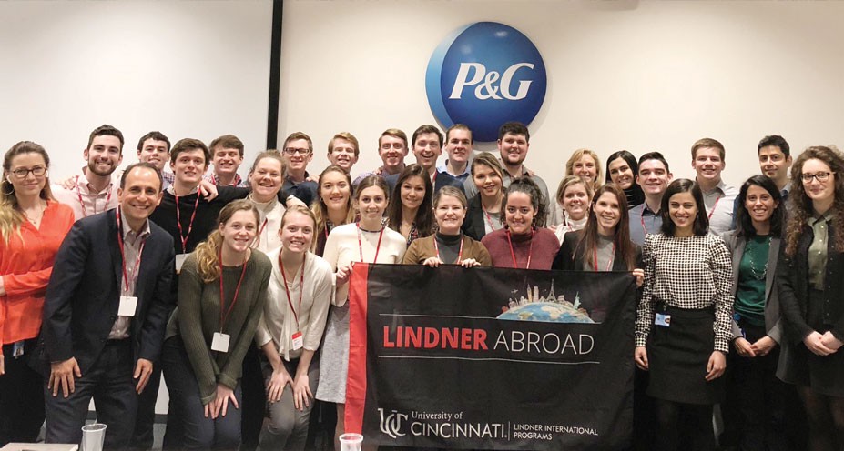 Lindner students and faculty pose with a "Lindner Abroad" flag in front of a P&G logo in Switzerland
