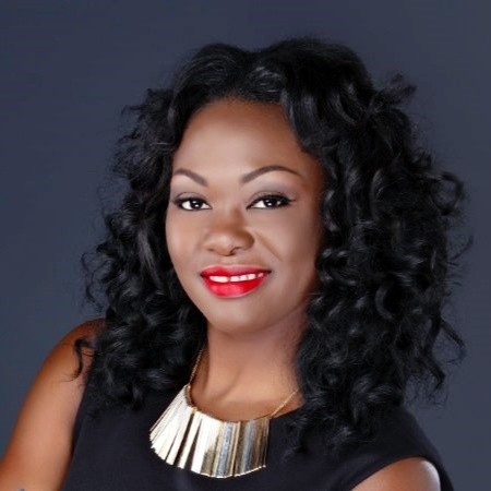 Hlack woman with black curly hair smiles for headshot wearing black sleeveless blouse and gold necklace