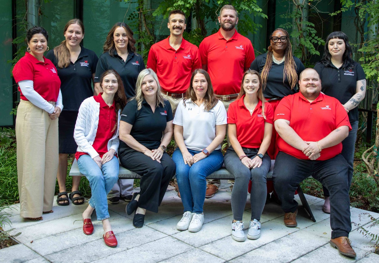 A group of men and women stand and sit in a courtyard, wearing red, black and white shirts and professional dress.