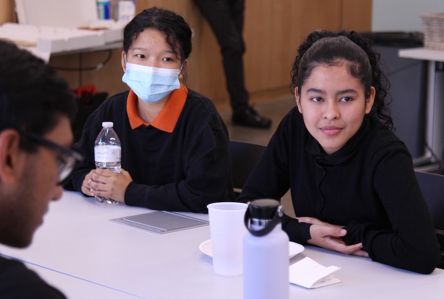 Two young women wearing black sweaters sit at a white table in a classroom in Lindner Hall