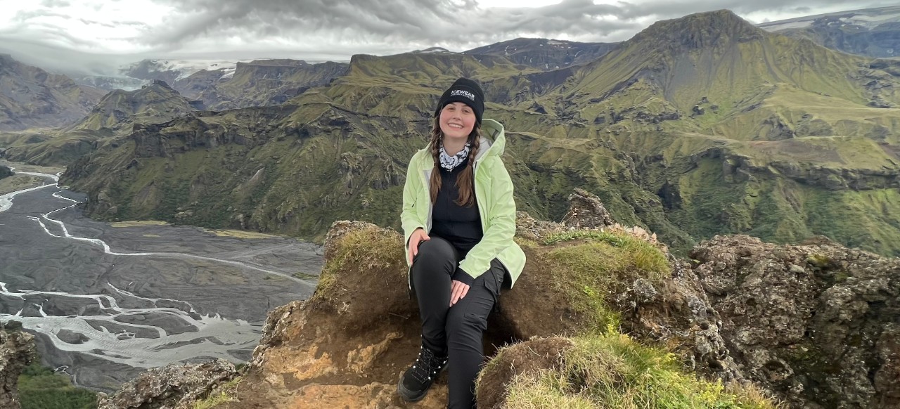 UC student sitting on mountaintop overlooking valley.