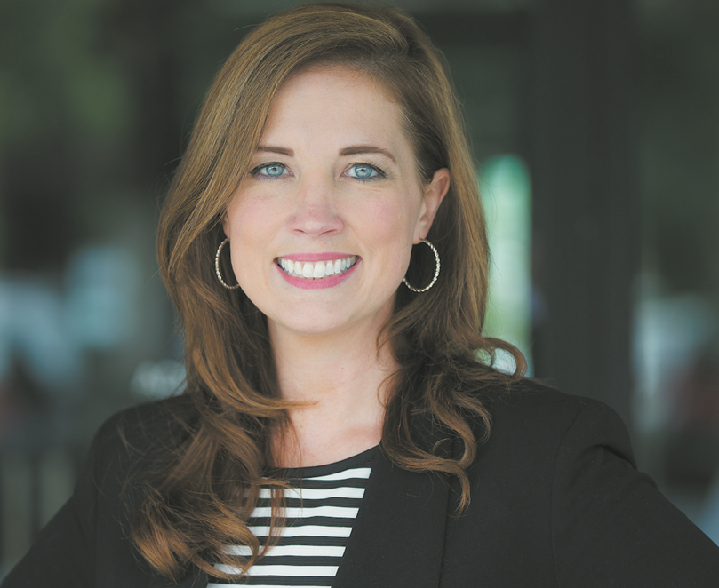 A woman smiles in a black jacket and striped shirt.